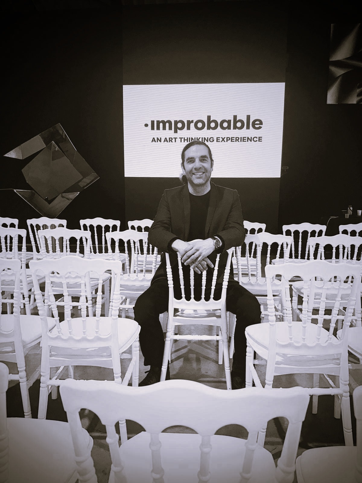 Sylvain Bureau 坐在白色座椅間,身後為 Improbable 標誌
